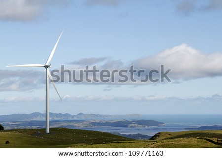 Giant wind turbine on hill and sheep grazing. Coastline in background