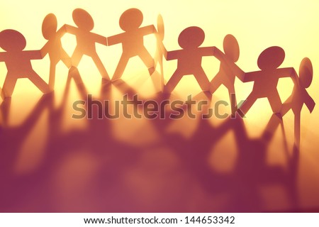 Team of paper doll people holding hands - stock photo