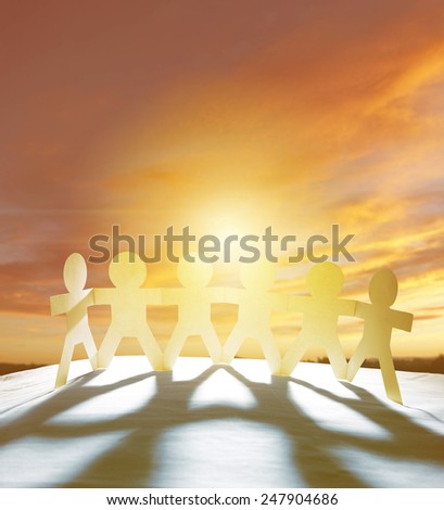 Team of six paper-chain people holding hands in front of bright sky