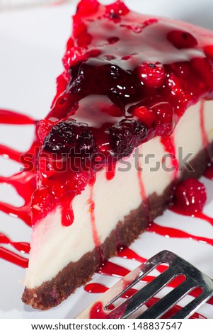 A delicious piece of cheesecake with berries and berry sauce on a white porcelain plate with a design  cake spoon