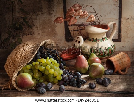 Autumn setting, wooden table and old wall with straw hat, grapes and pears, decorative dried flowers and red gourd