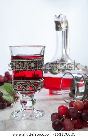 Red wine in vintage crystal and silver glassware, a crystal and silver decanter and red grapes besides.