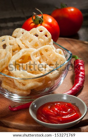 Fried potato chips in transparent glass bowl, with hot salsa, fresh tomatoes and chili peppers on a wooden cutting board