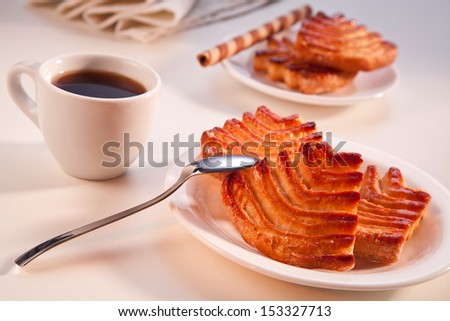 A cup of black coffee and pastry on a white porcelain plate, more pastry in the background and a white cloth napkin