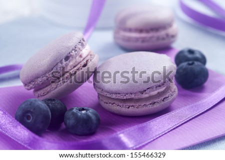 Violet French macaroons cookies and blueberries on violet fabric with violet ribbon  on horizontal