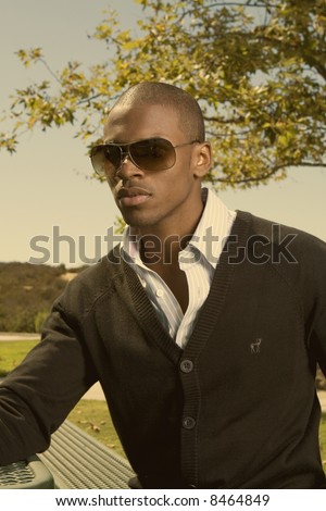 wealthy young black man sitting in a park with sun glasses