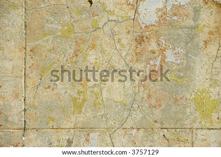 Cracked concrete wall with peeling paint of different colours/colors and lines scored to look like sandstone bricks for use as background.