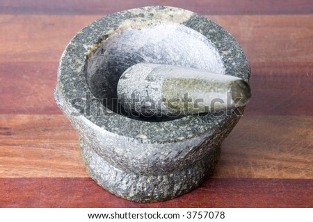 Stone mortar and pestle on a weathered wooden chopping board with the pestle placed in the mortar
