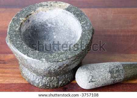 Stone mortar and pestle on weathered wooden chopping board with pestle next to the mortar