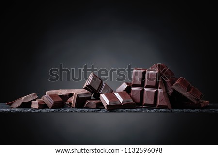 Broken chocolate pieces on a black background. Copy space.