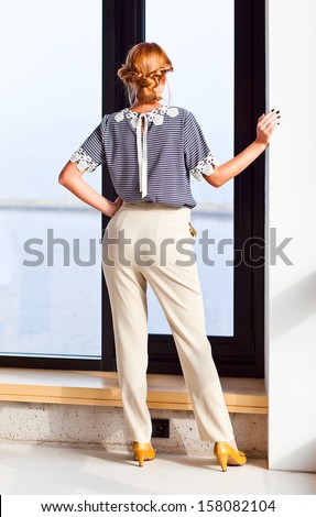 The young beautiful woman in striped blouse before a window