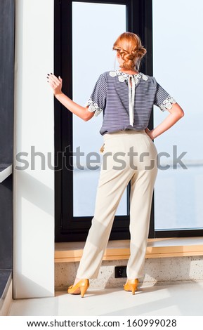 The young beautiful woman in striped blouse before a window