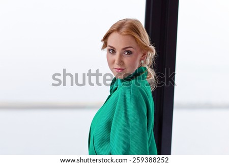 The young beautiful woman in green jacket before a window
