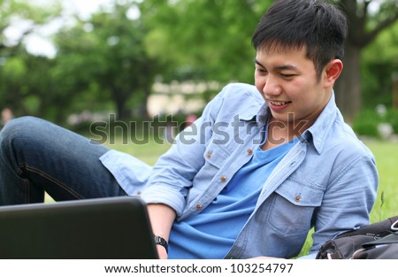 college student with laptop laying on the grass smiling