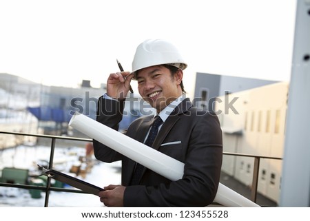 young architect with white helmet holding blueprint and clipboard smiling look at the camera