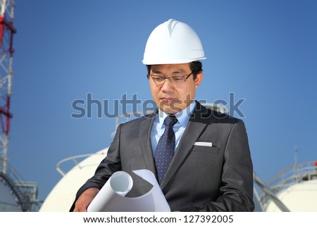 engineer oil refinery checking plan on location site with tower and blue sky background