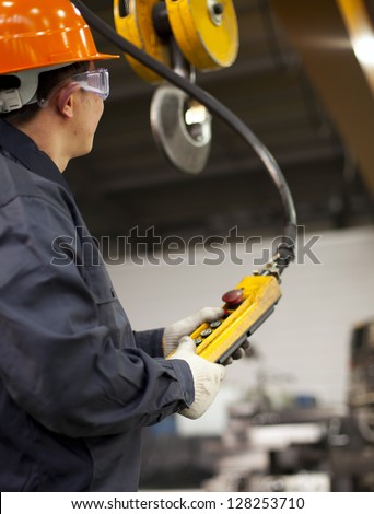 Worker holding crane hook button working in factory with safety work-wear