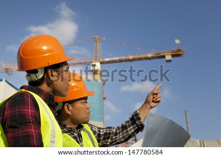 Construction worker wearing protective clothing discussion on location site and yellow crane on the background