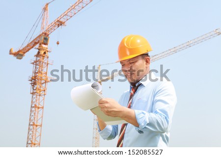 Construction worker manager holding a notepad with cranes on the background