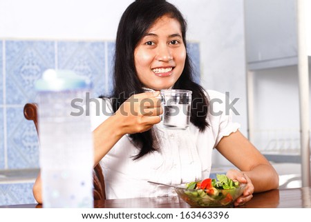 Portrait of smiling young woman drinking water with salad on table