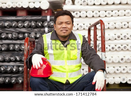 Textile factory worker sitting beside  raw material fabrics stacked