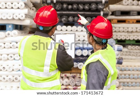 Two workers factory textile inspecting and checking raw material fabrics in warehouse
