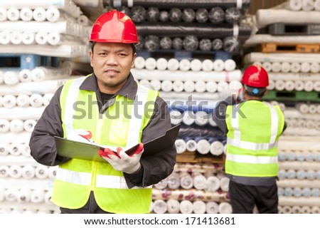 Portrait textile factory worker holding notepad with partner working on the background