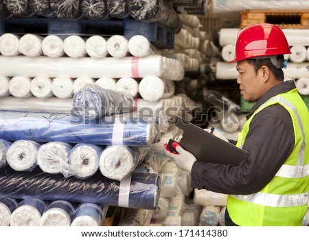Textile factory foreman auditing raw material fabrics in warehouse