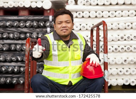 Textile factory worker sitting under raw material fabric with giving thumb up