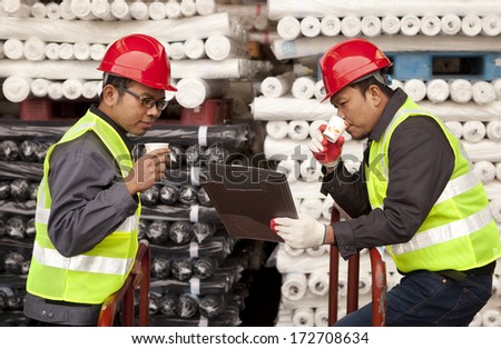 Textile factory workers discussing in warehouse fabric with drinking coffee