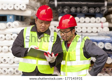 Textile factory workers discussing with stacked fabric on background