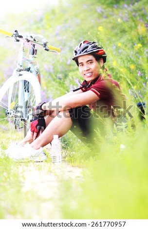 Happy man cyclist sitting on grass and flower resting