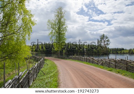 Springtime view from an old gravel road with wooden fence by a small lake