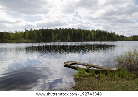 Water filled old wooden rowing boat by a small lake at springtime