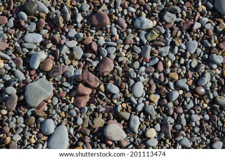 Background of smooth and wet gravel and pebbles at a beach in soft lighting