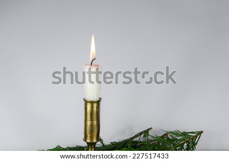 One burning white candle in a candlestick of bronze at a white wall