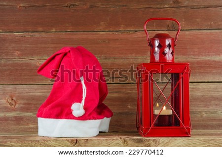 Santa Claus equipment red cap and Christmas lantern at a background of an old weathered wooden plank wall