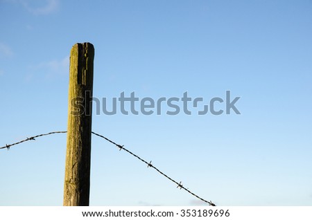 Fence post with old barb wire at blue sky