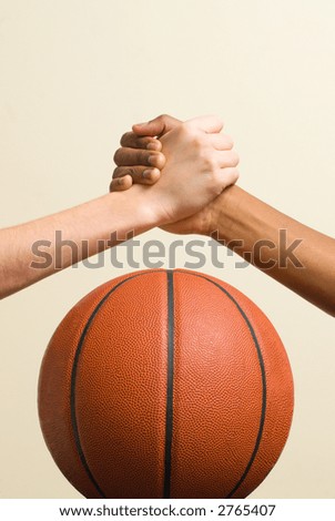 White teen and Black teen clasp hands over a basketball.