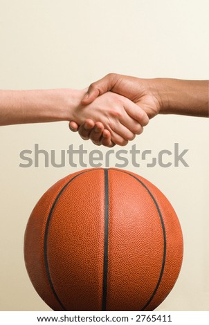 White teen and Black teen shake hands over a basketball.