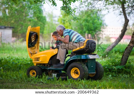 image of grandfather and grandson at sunset checking lawn mower