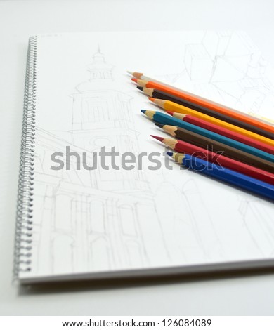 Pencil sketch of buildings on white paper lies with color pencils