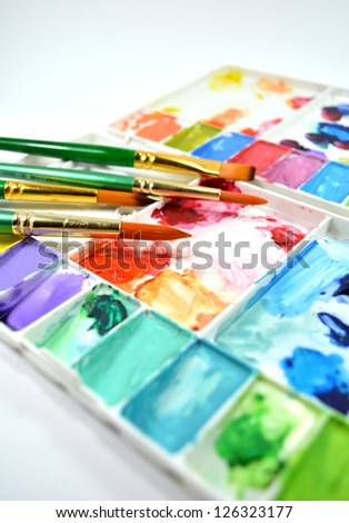 Colorful watercolor palette and different type of paintbrushes on white background