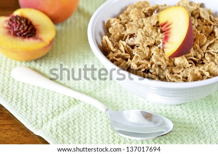 A bowl of cereal , slices of peach and a spoon on a table
