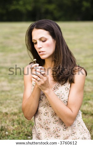 Woman in sun dress gazing at a small flower in her hands