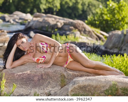 Brunette girl in bikini laying on rocks