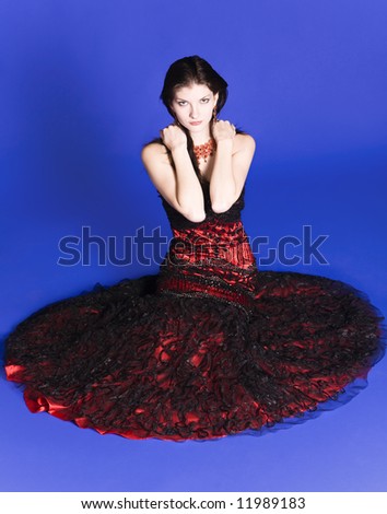Beautiful young woman wearing a red evening gown sitting on the floor