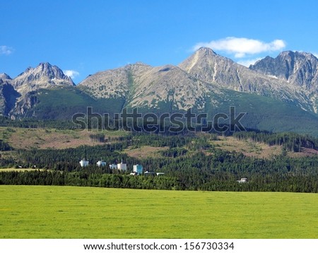 Mountain chain of High Tatras with green meadow and small block of flats under their huge peaks. High Tatra mountains are most popular tourist destination in Slovakia during all seasons.