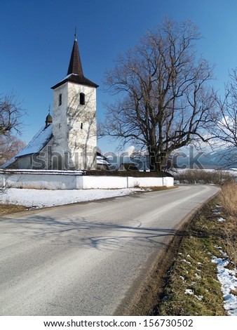 Winter view of road leading to All Saints church in Ludrova village, near Ruzomberok town, northern Slovakia. This rare Gothic church is oldest sacral construction in region of Liptov.