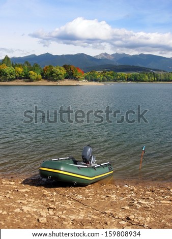 Vertical autumn view portraying waters of Liptovska Mara lake with small inflatable fishing boat anchored on its shore and dominant Rohace hills, part of Western Tatras in background.